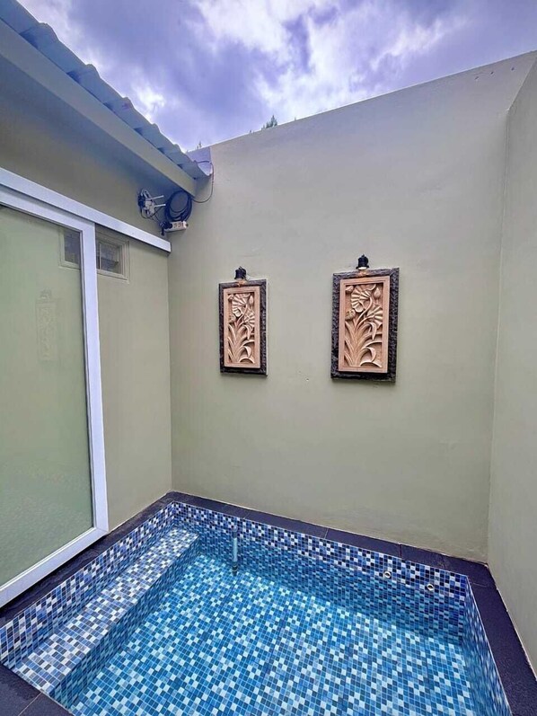 A small indoor swimming pool with blue and white mosaic tiles, surrounded by a light-colored wall with two decorative panels. - Diiza Glamping Tawangmangu (Tawangmangu)