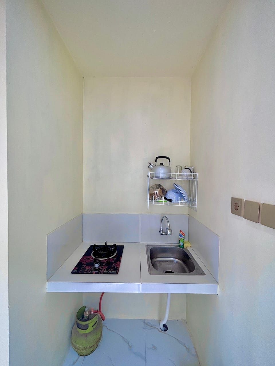 Una piccola cucina con un fornello a gas, un lavello e uno scaffale sopra il lavello con piatti e un bollitore.