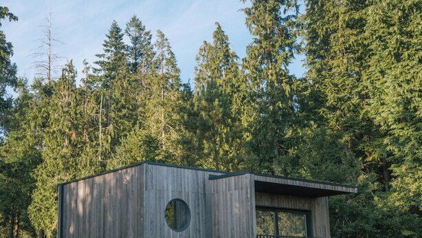 A wooden cabin with a circular window and a balcony, surrounded by a forest. - Bungalows da Travanca (Arcos de Valdevez)