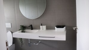 A modern bathroom with a white sink, black faucet, and a round mirror. - Bungalows da Travanca (Arcos de Valdevez)