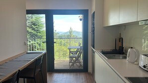 A compact kitchen with a dining area, a balcony with a table and chairs, and a view of greenery and mountains. - Bungalows da Travanca (Arcos de Valdevez)