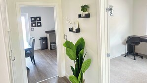 A hallway with a dining area, a large green plant, and a desk with a chair.
