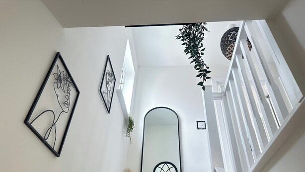 A staircase with white railings, a wall-mounted mirror, and two framed artworks.
