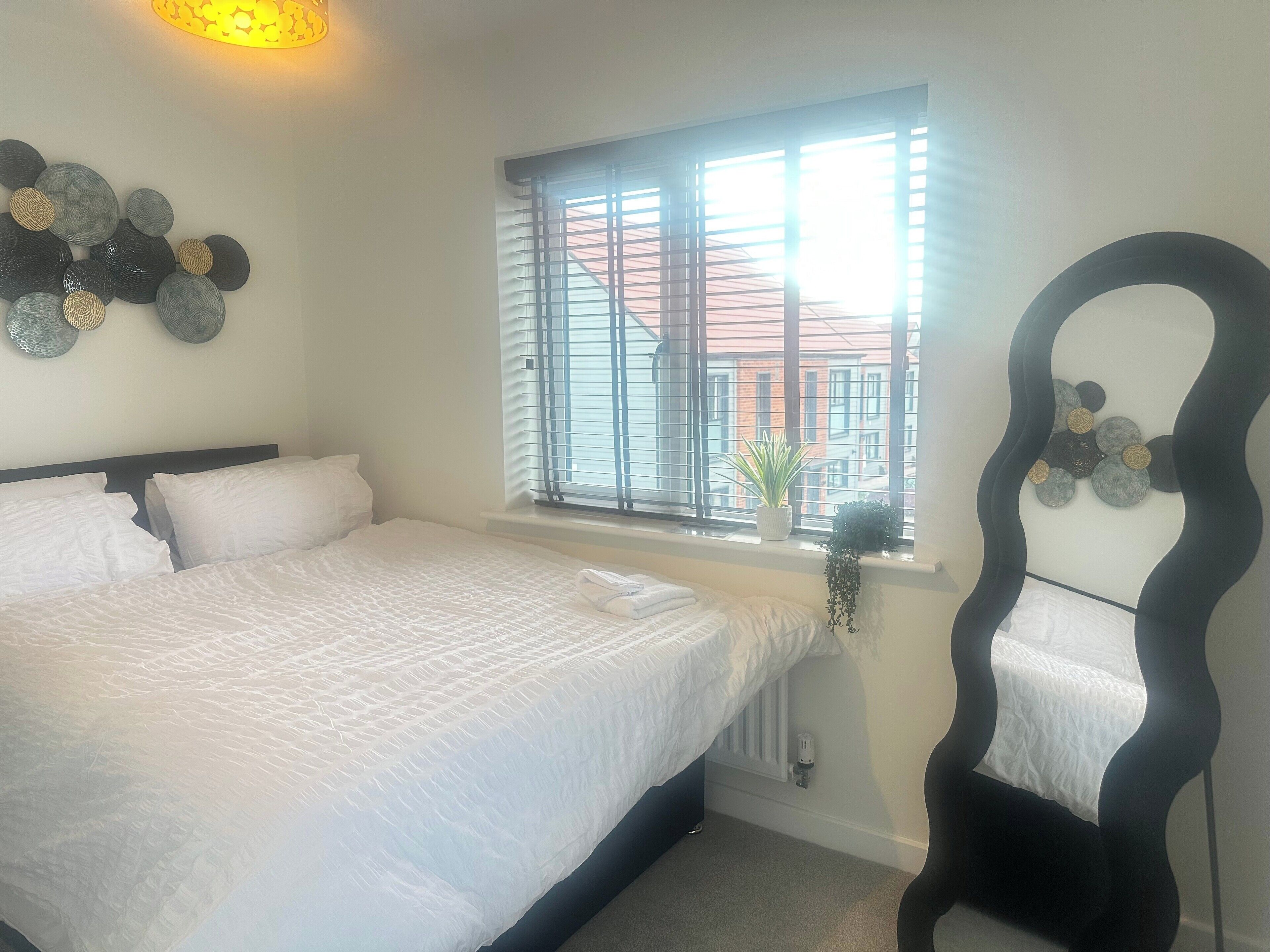 A bedroom with a large bed, a window with blinds, a radiator, and a unique chair design.