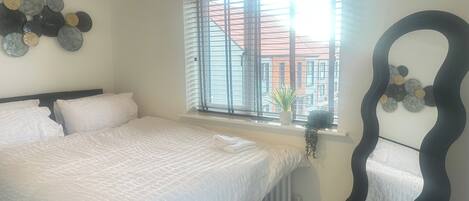 A bedroom with a large bed, a window with blinds, a radiator, and a unique chair design.