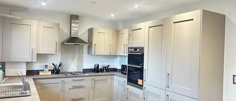 A modern kitchen with light-colored cabinets, a stainless steel range hood, a built-in oven, and a coffee maker on the countertop.