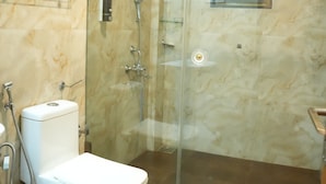 A bathroom with a glass-enclosed shower, a toilet, and a marble wall. - Rio Royale Resort (Karjat)