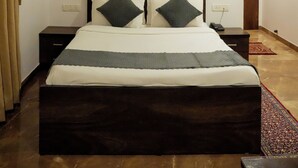 A bedroom with a wooden headboard, a bed with two pillows, a nightstand, a wall-mounted air conditioner, a framed picture, and a ceiling fan. - Rio Royale Resort (Karjat)