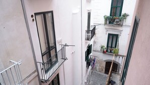 Un estrecho callejón entre edificios con balcones, algunos adornados con plantas y ropa tendida.