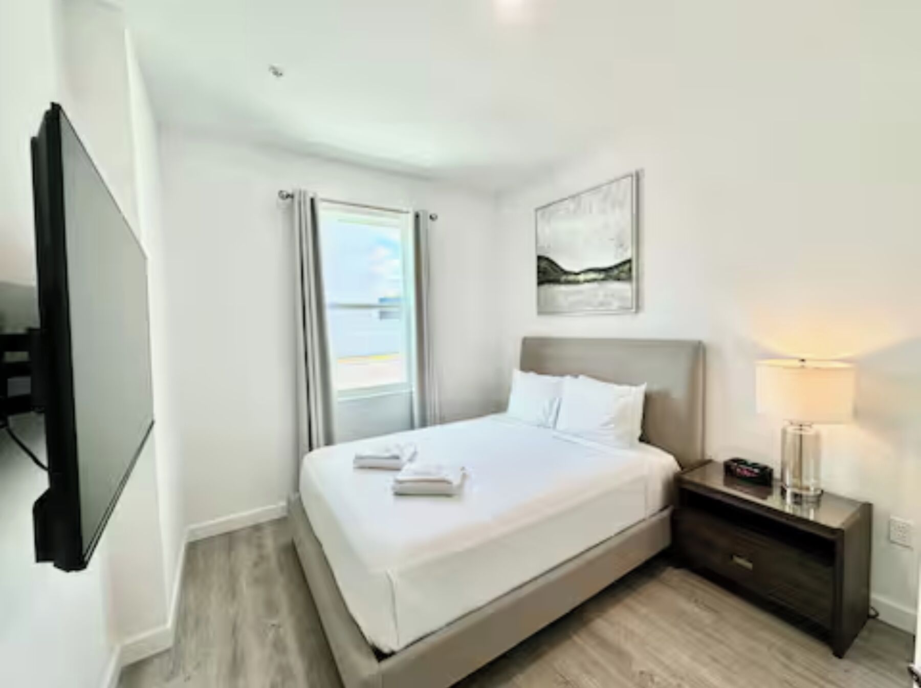 A hotel room with a bed, a nightstand, a lamp, and a painting on the wall.
