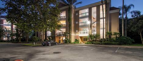 A multi-story building with a central atrium, surrounded by palm trees and a parking lot.