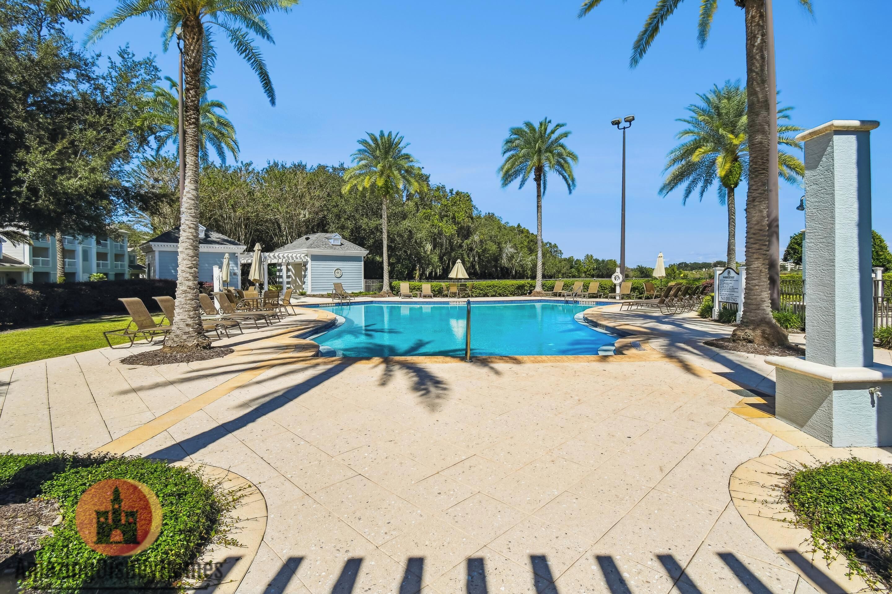 A pool area with lounge chairs, palm trees, and a clear blue sky.