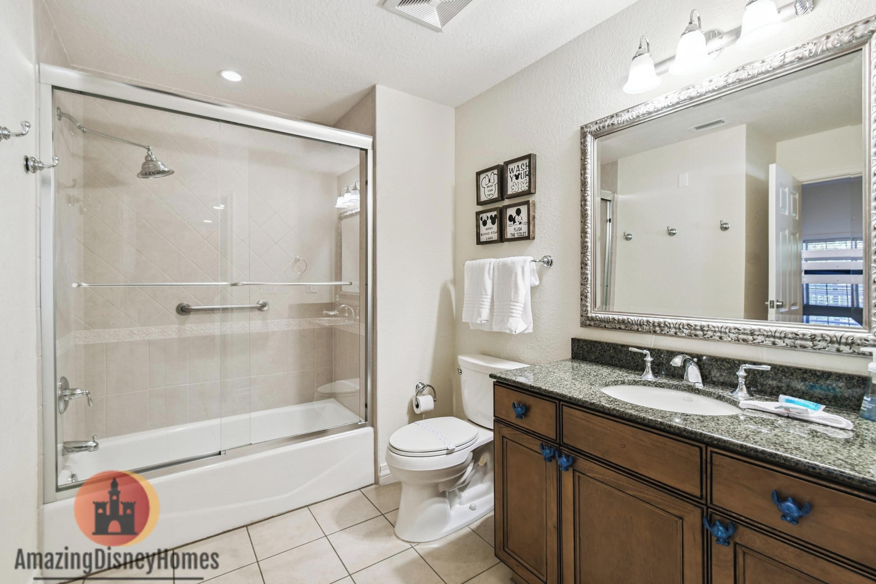 A bathroom with a glass-enclosed shower, a white toilet, a sink with a vanity, and a large mirror.