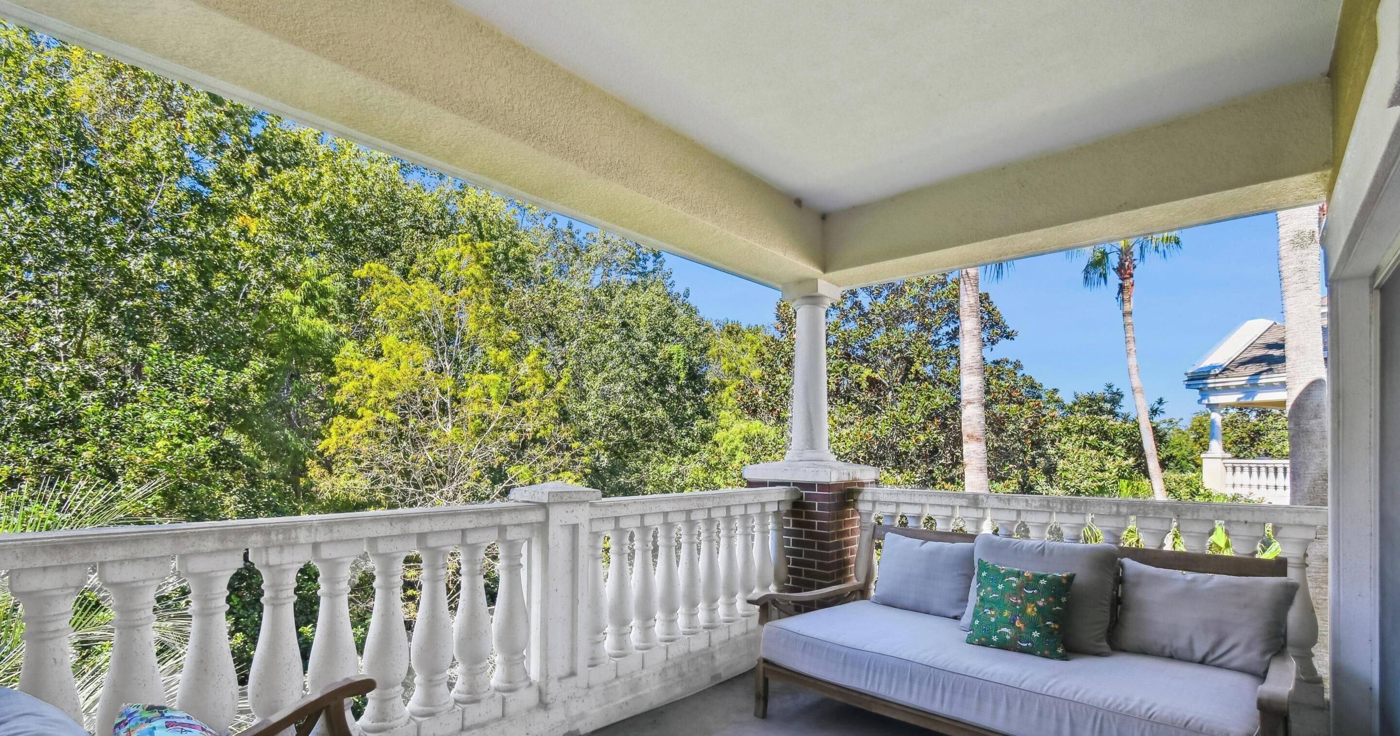 A covered outdoor seating area with a white balustrade, a white sofa with cushions, and a wicker chair.