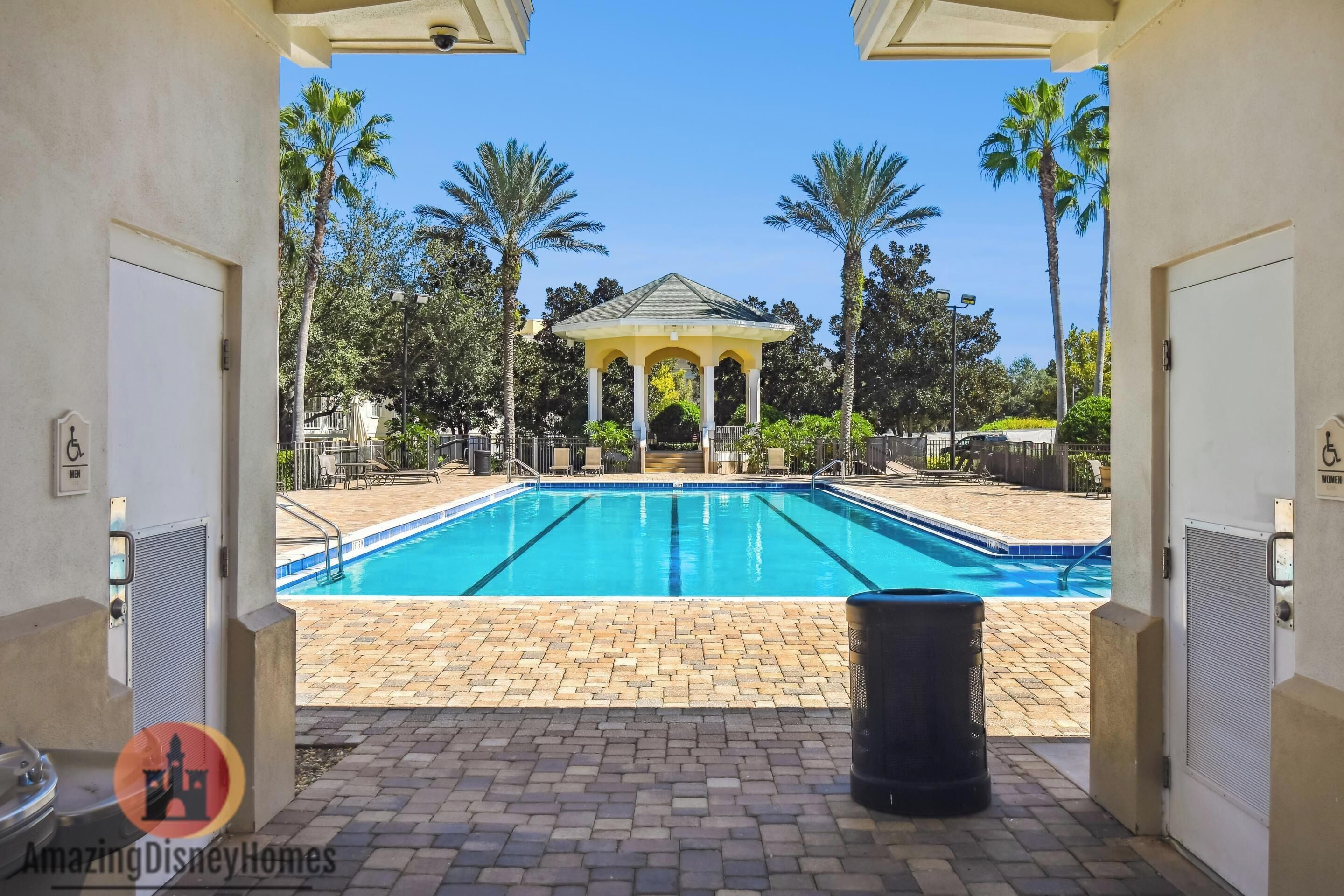 A swimming pool with a gazebo in the background, surrounded by palm trees and a clear sky.