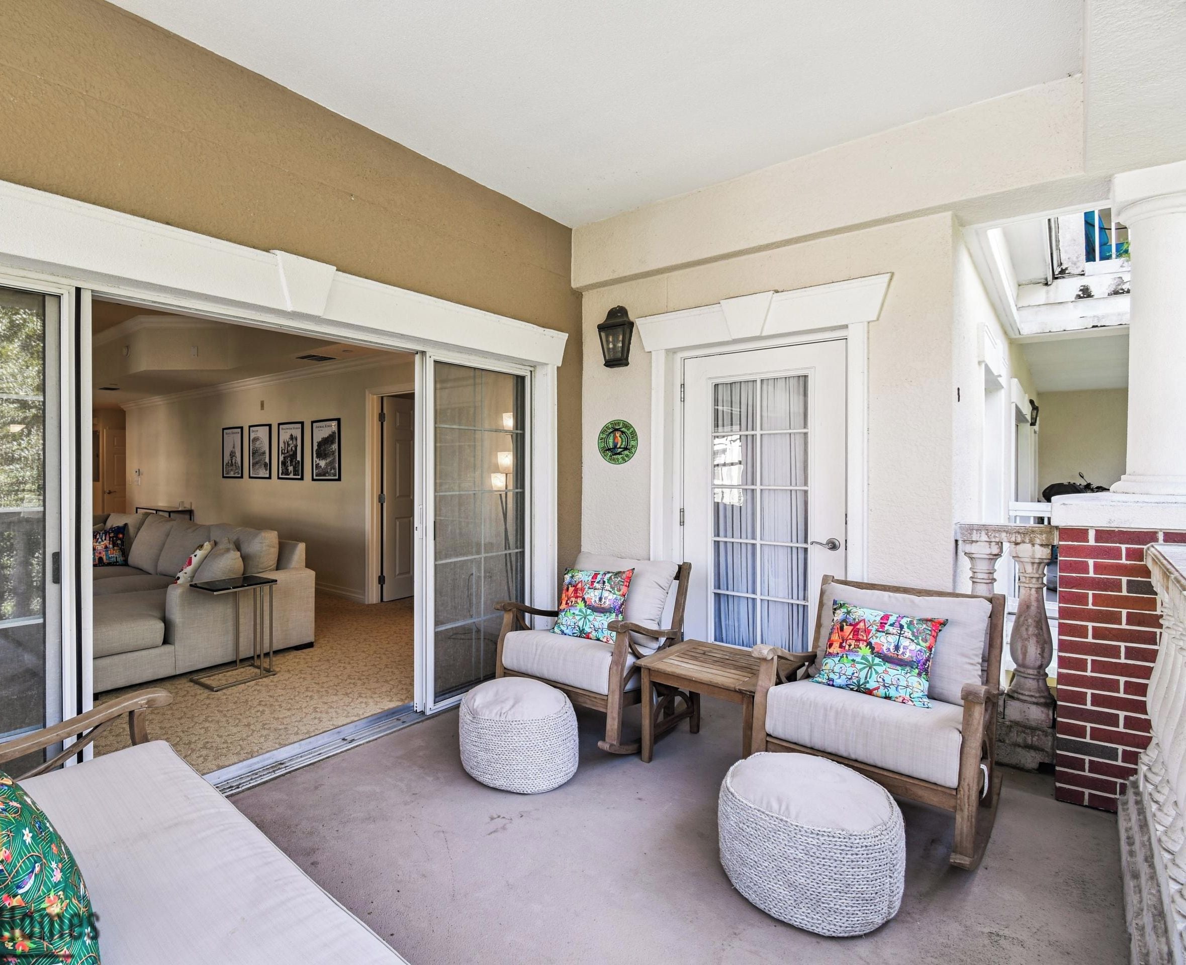 A covered patio area with sliding glass doors leading to an interior living space, furnished with a sofa, chairs, and ottomans.