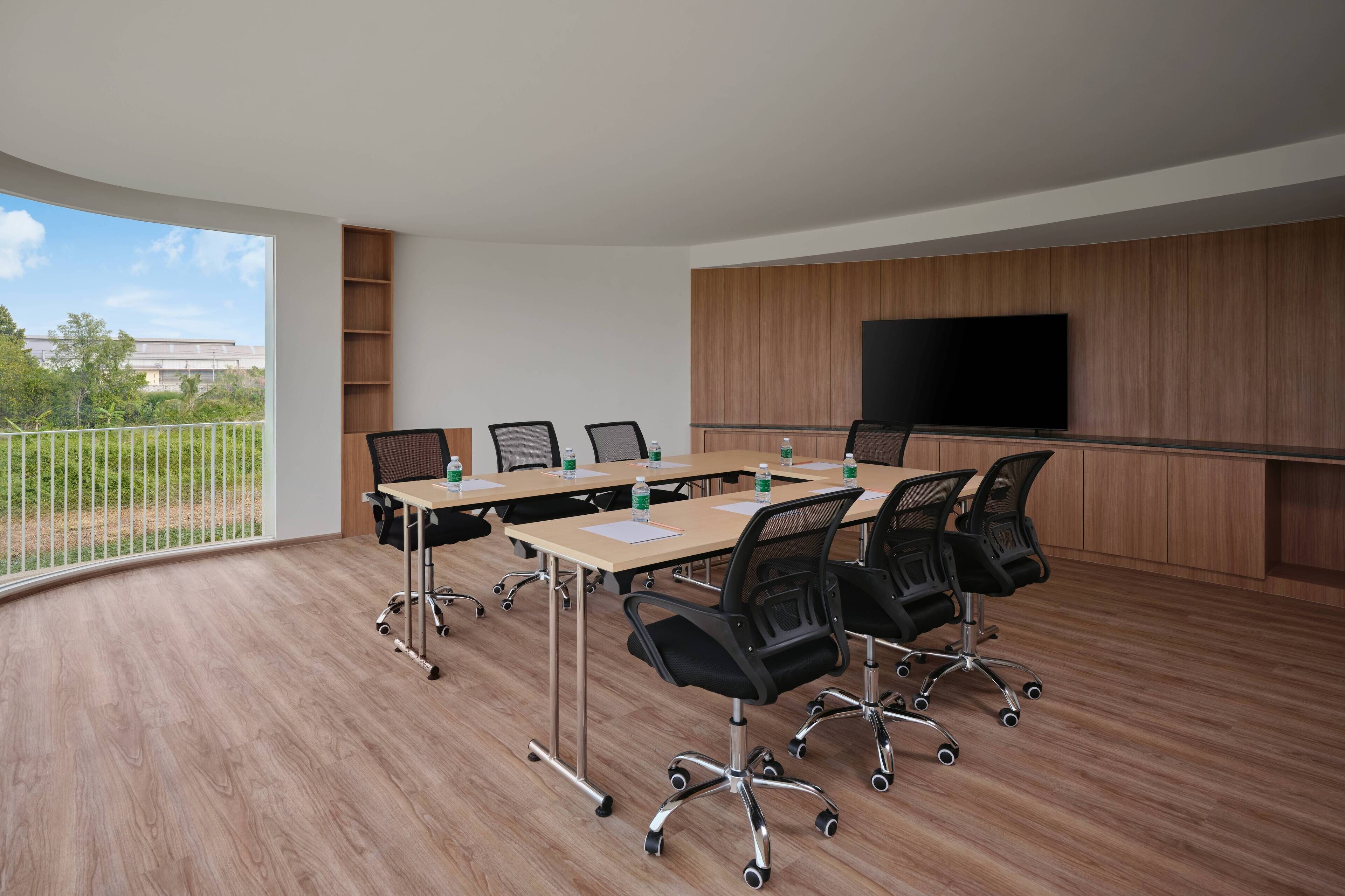 A conference room with a large table, multiple chairs, a television, and a view of greenery outside.