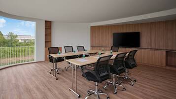 A conference room with a large table, multiple chairs, a television, and a view of greenery outside.
