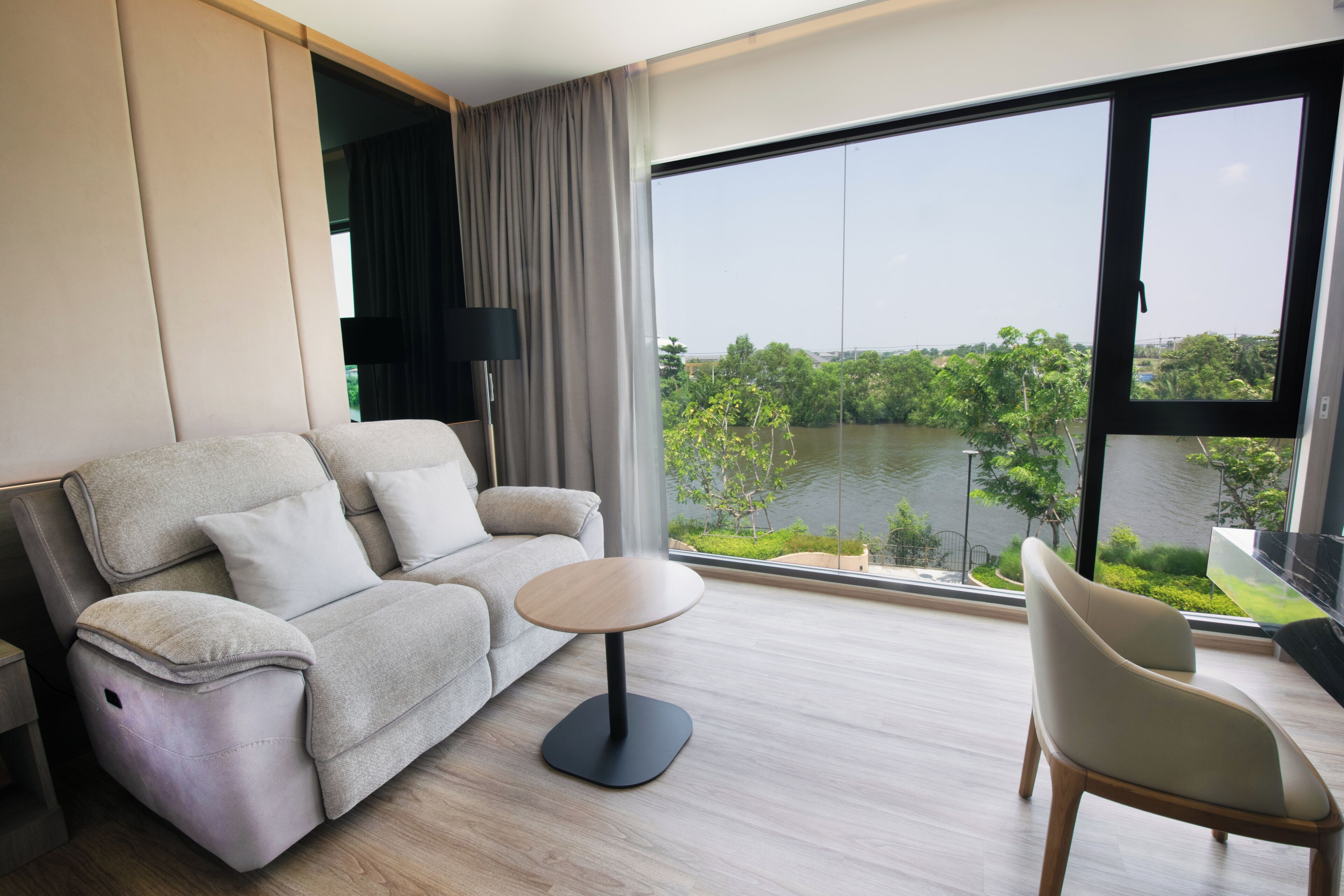 Un moderno salón con un sofá, una mesita redonda y vista a un cuerpo de agua a través de amplias ventanas.