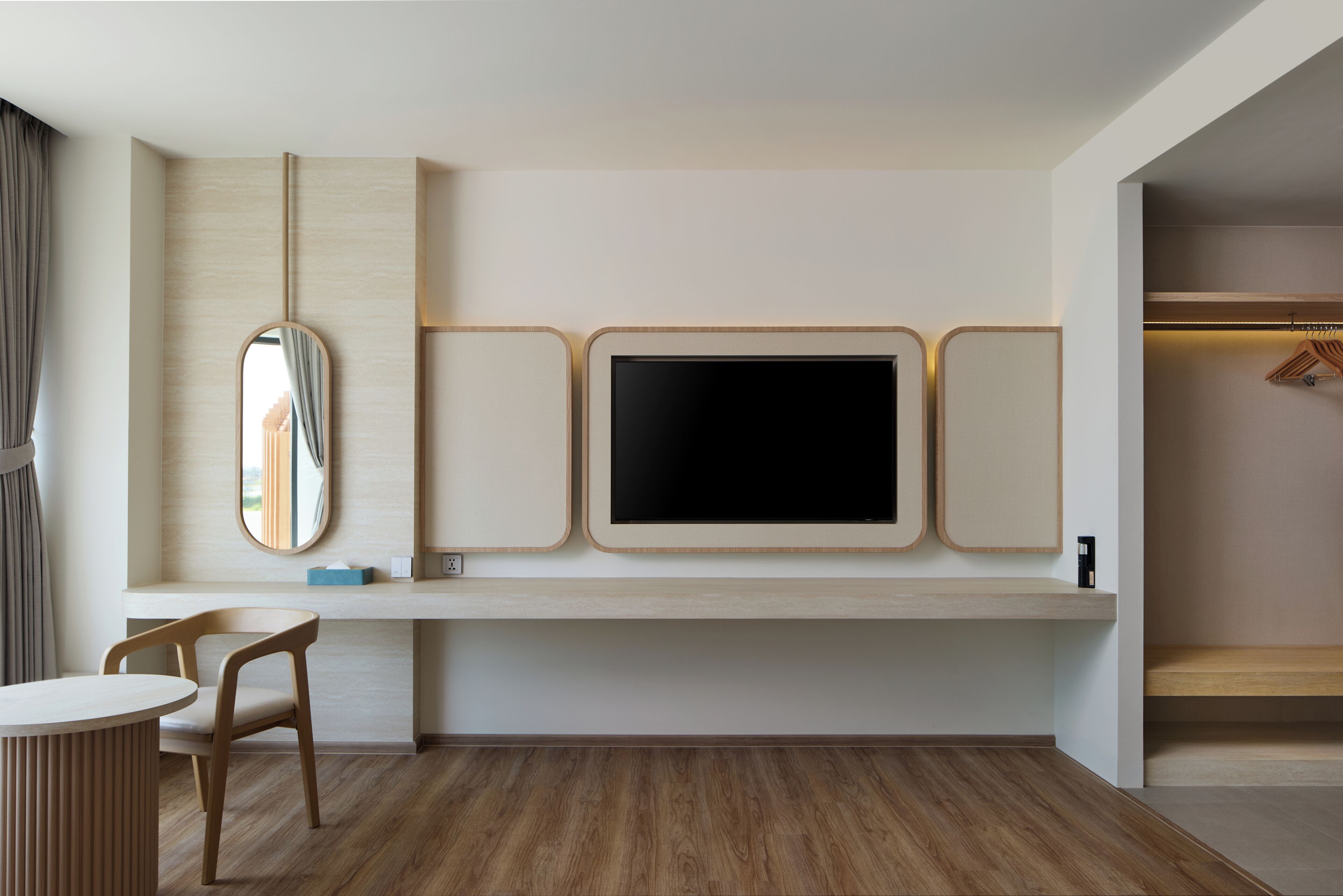 A modern room with a wooden floor, a desk with a chair, a large mirror, and a TV on a wall.