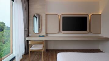 Habitación de hotel con cama, escritorio con silla, un espejo grande y televisor montado en la pared.