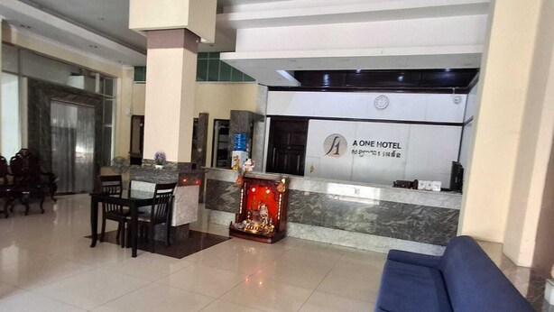 A hotel lobby with a reception desk, a blue sofa, and a dining area with chairs.