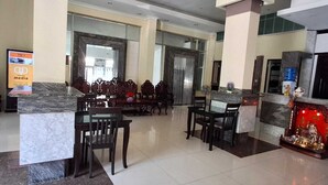 A hotel lobby with marble flooring, wooden furniture, a reception desk, and a television screen.