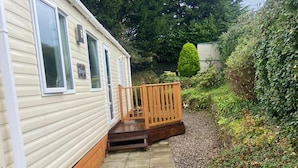 A mobile home with a wooden deck and a gravel pathway leading to the entrance. - 2 Bed Caravan-sleeps 6-pet Friendly (Carnforth)