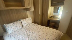 A bedroom with a bed, a wooden wardrobe, a small desk, and a mirror. - 2 Bed Caravan-sleeps 6-pet Friendly (Carnforth)
