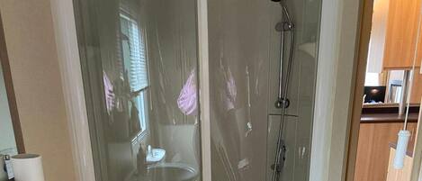 A glass-enclosed shower with a handheld showerhead and a wall-mounted faucet.