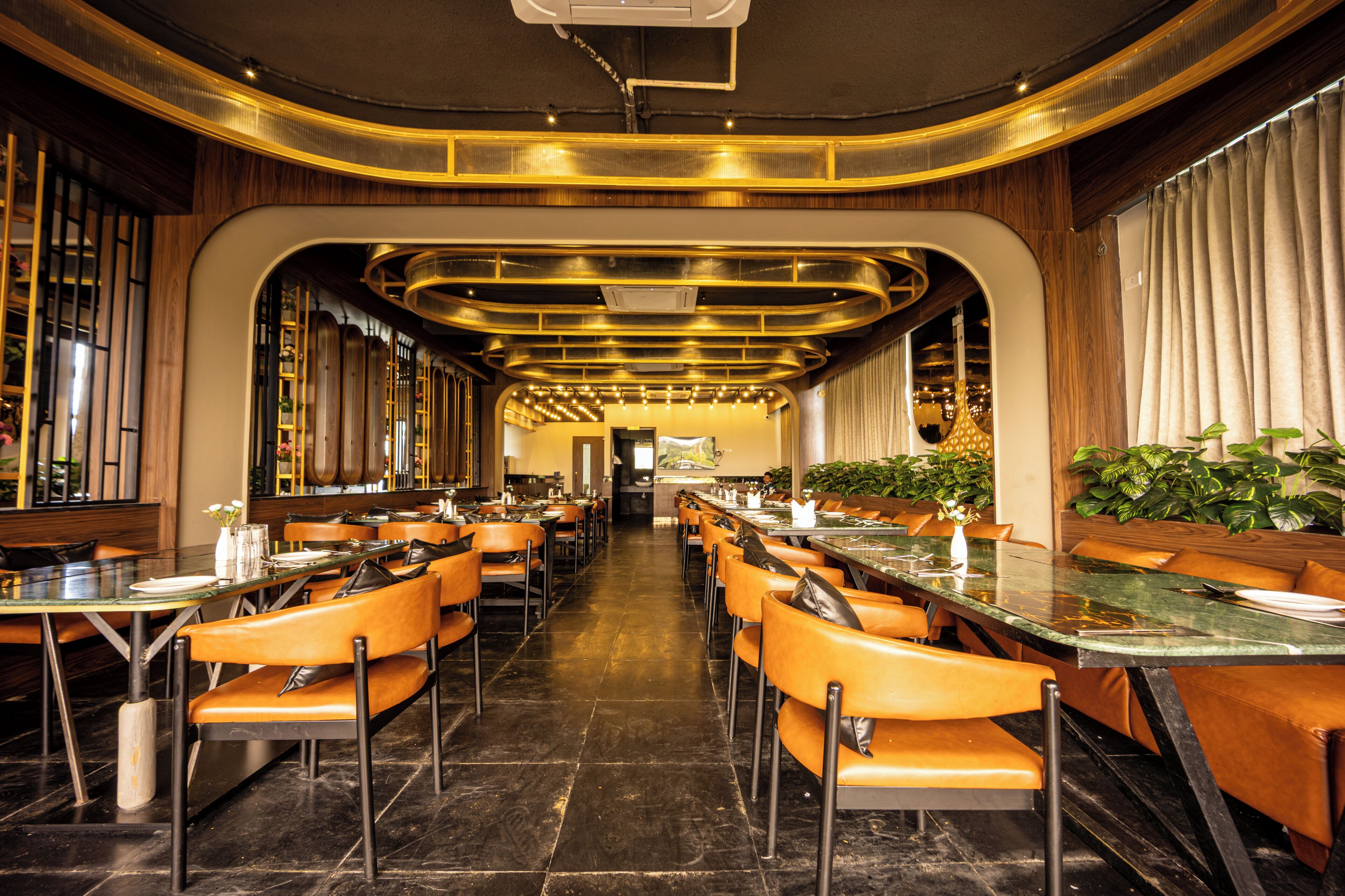Un restaurant avec de longues tables et des chaises orange, un sol en marbre et un plafond au design moderne.