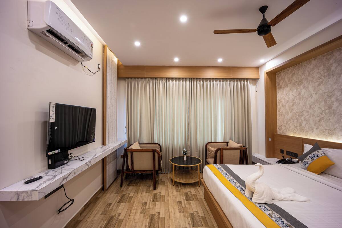 Habitación de hotel con una cama, televisión, ventilador de techo y una mesita con un florero.