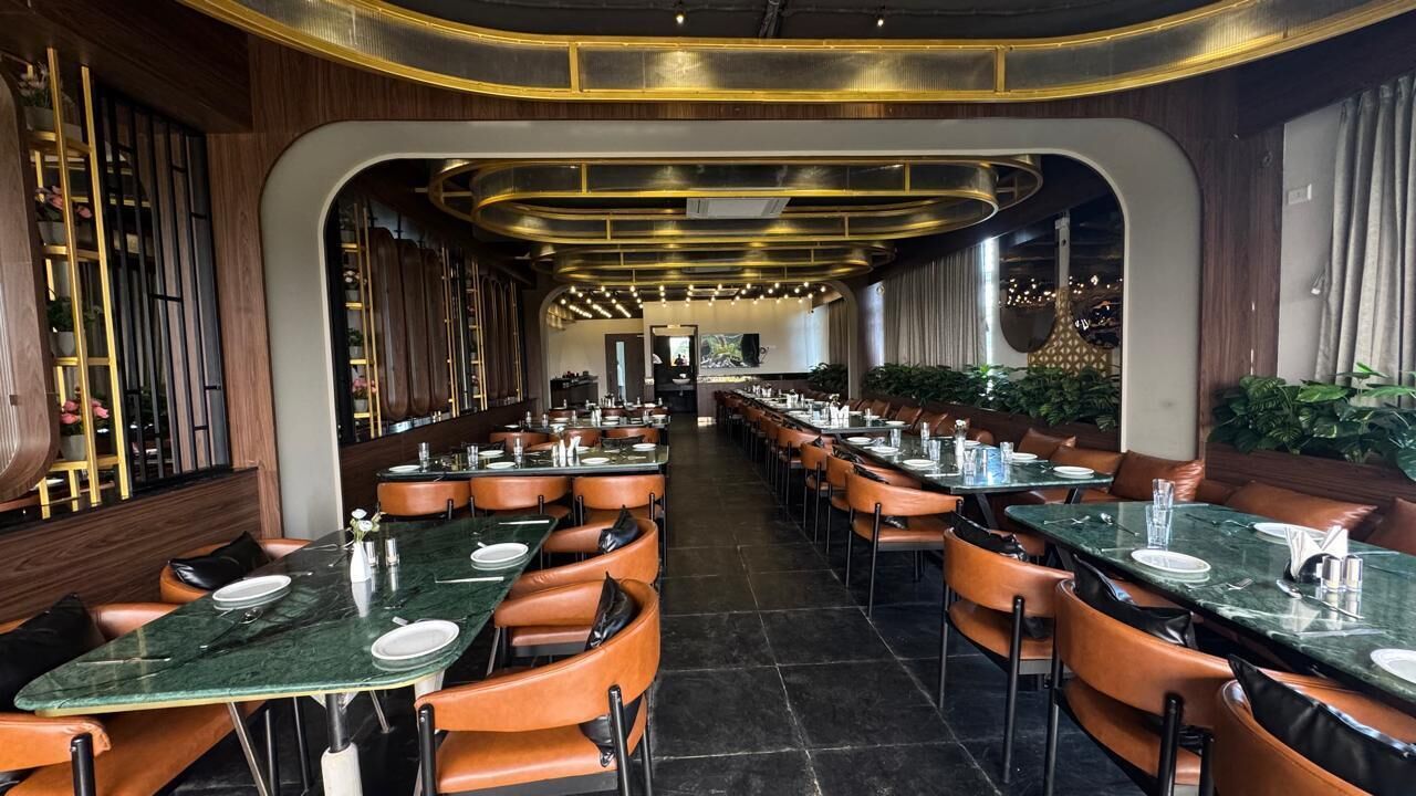 A restaurant with long tables and booths, wooden paneling, and a modern chandelier.