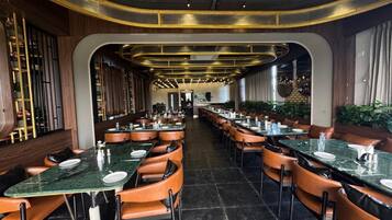A restaurant with long tables and booths, wooden paneling, and a modern chandelier.