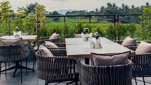 Une terrasse extérieure aménagée avec des chaises et des tables en osier, offrant une vue sur un paysage luxuriant et des collines lointaines.
