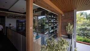 Un espace bar moderne avec un plafond en bois, des rampes de protection en verre et une vue sur la verdure environnante.