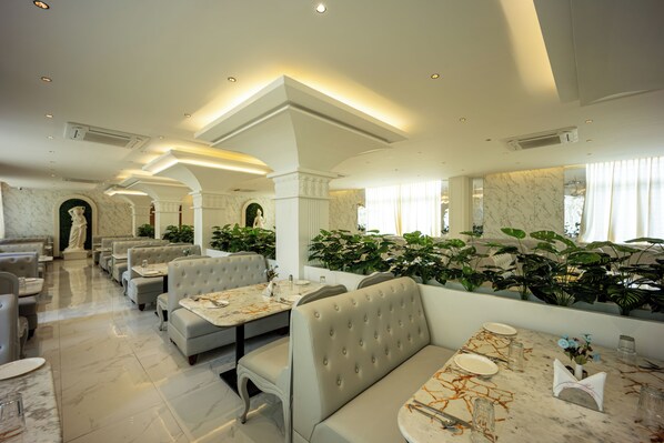 A spacious restaurant with marble flooring, cushioned seating, and a large plant wall.