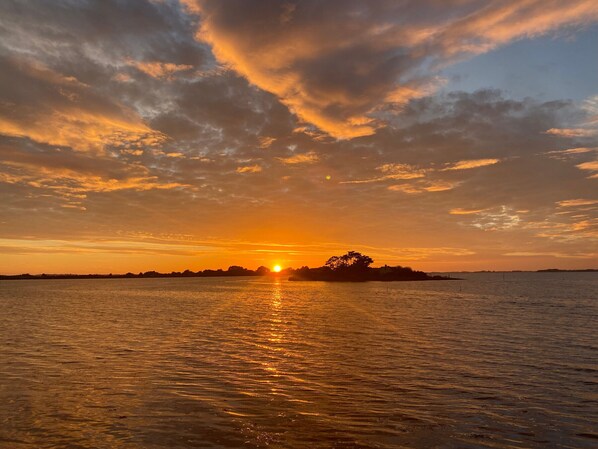 A sunset over a calm body of water with a distant landmass silhouetted against the sky.