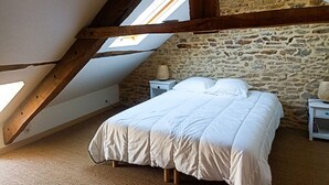 Une chambre avec un mur en pierre, un lit, une table de chevet et une lucarne.