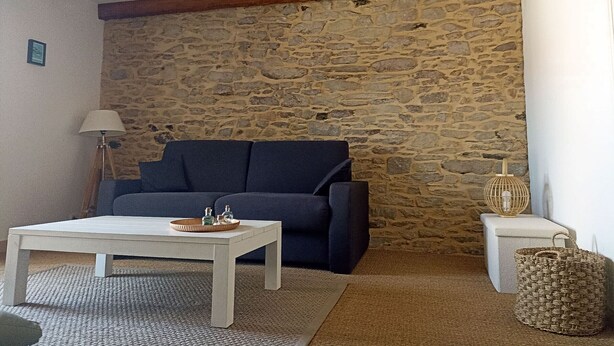 Un salon chaleureux avec un mur en pierre, un canapé bleu foncé, une table basse blanche et une lampe.
