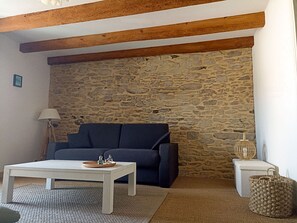 A cozy living room with a stone wall, a dark blue sofa, a white coffee table, and a lamp.