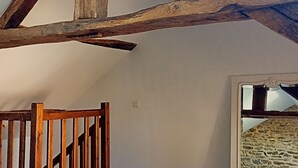 Une pièce avec des poutres apparentes, un escalier en bois et un mur de pierre visible à travers une porte.