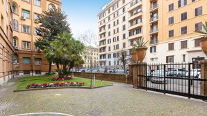 Un cortile con pavimentazione in pietra, un piccolo giardino fiorito e una recinzione in metallo nero.