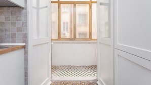 Una cocina estrecha con piso de tablones encalados, un ventanal con vidrio esmerilado y muebles blancos.