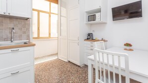 Cocina compacta con armarios blancos, microondas, cafetera y una pequeña mesa con una silla.