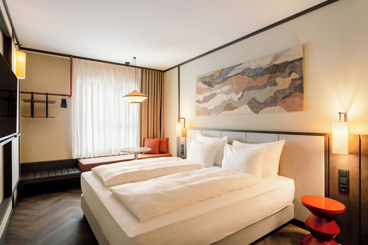 A hotel room with a large bed, a bench, a wall-mounted TV, and a painting.