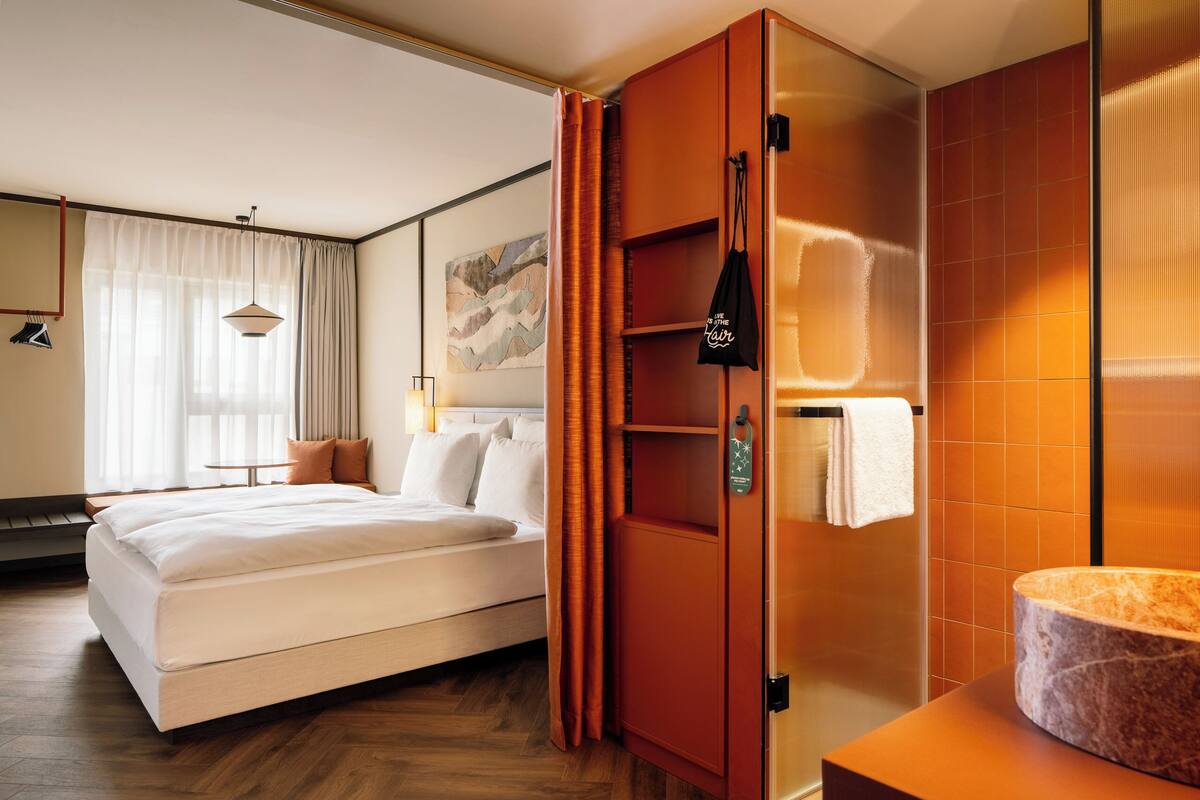A hotel room with a bed, a wardrobe, a bathroom with a marble sink, and a painting on the wall.