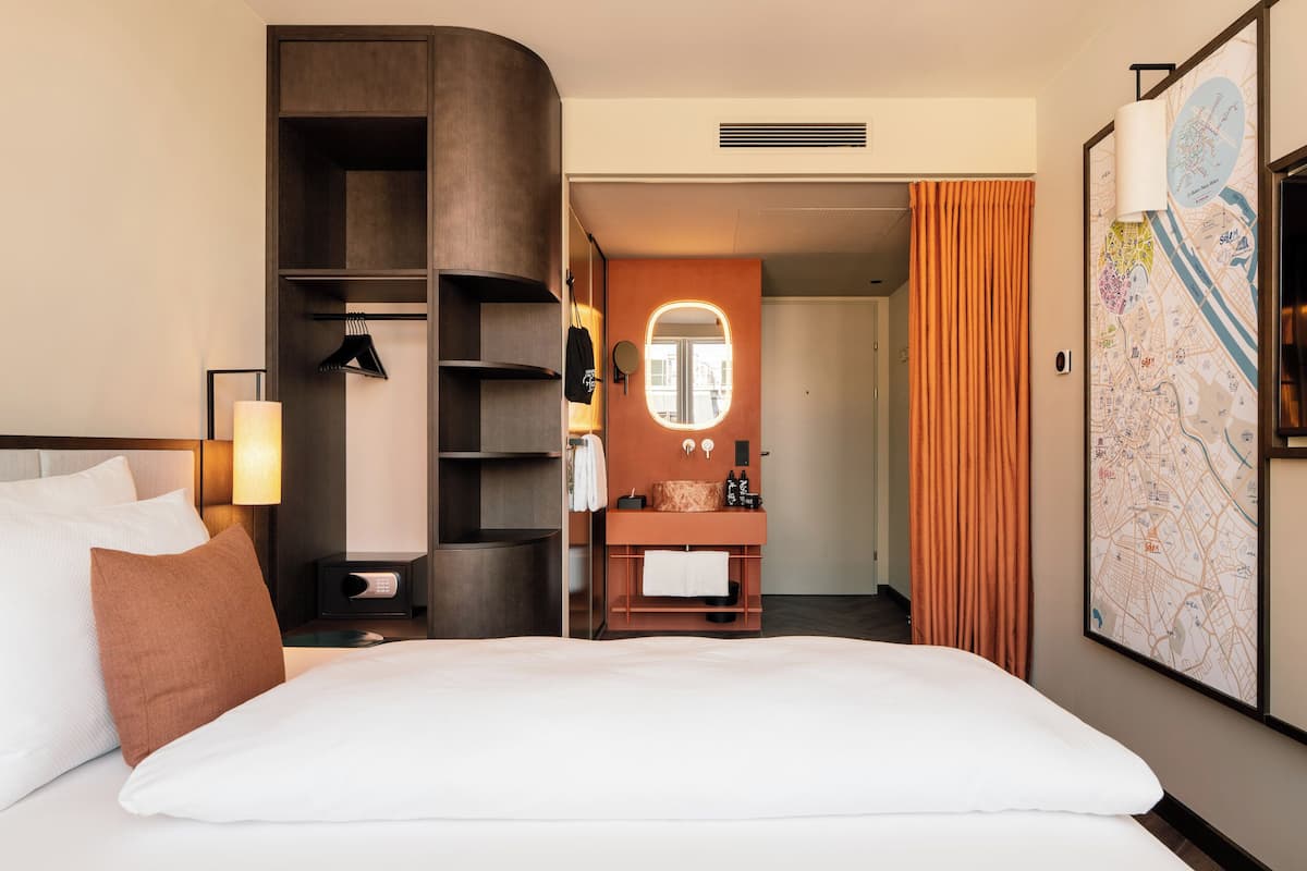 A hotel room with a bed, a nightstand, a mirror, a map on the wall, and a door leading to another room.