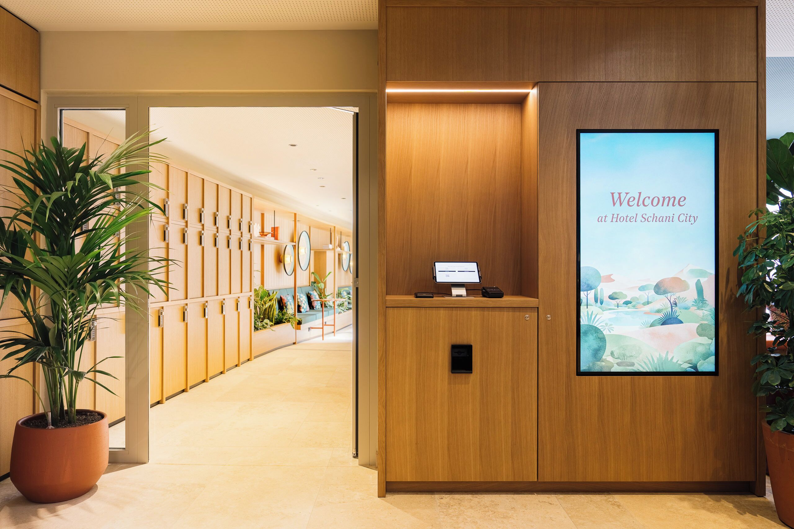 A reception desk with a welcome sign, a potted plant, and a corridor leading to rooms.