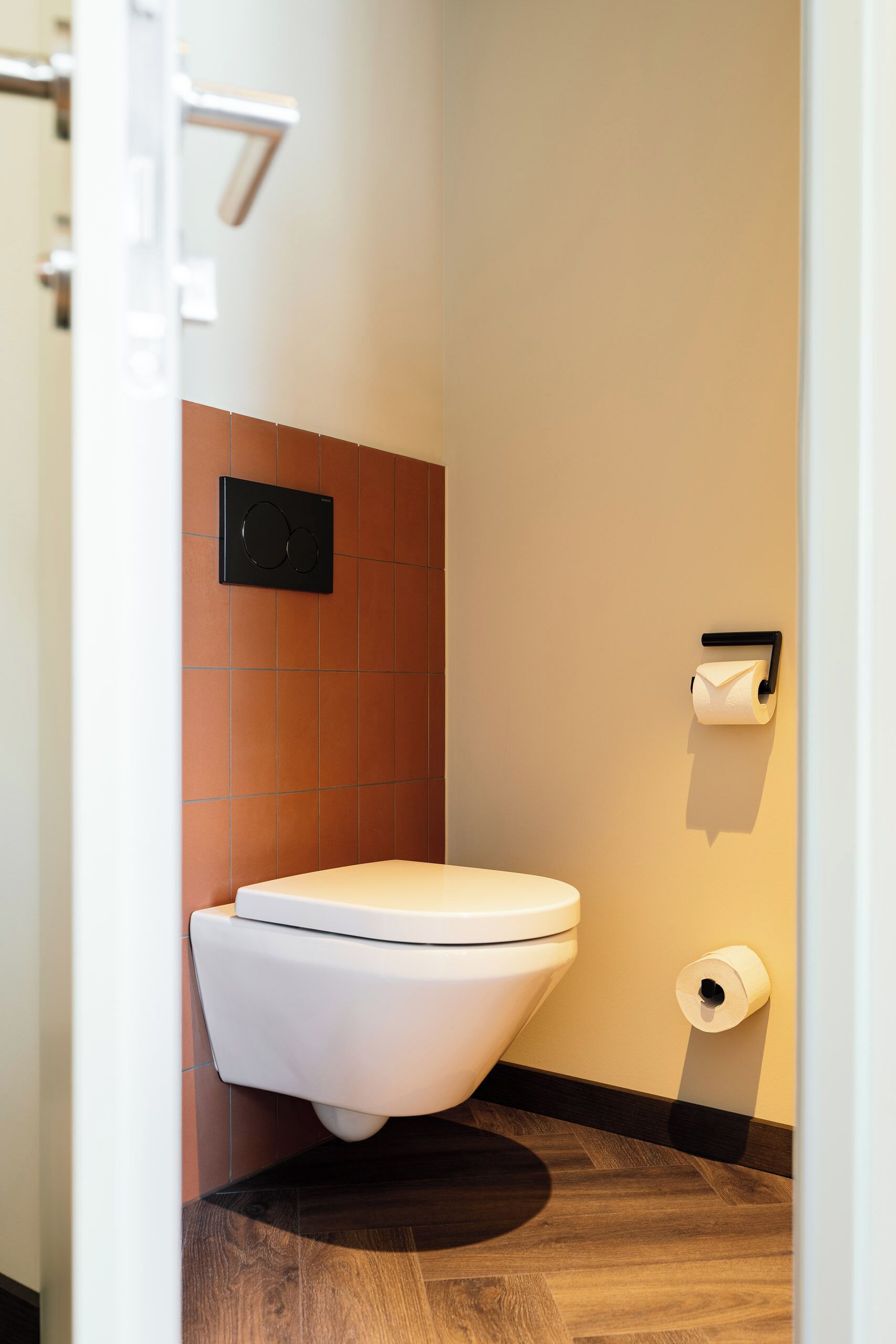 A modern bathroom with a toilet, a wall-mounted toilet paper holder, and a visible ventilation system.